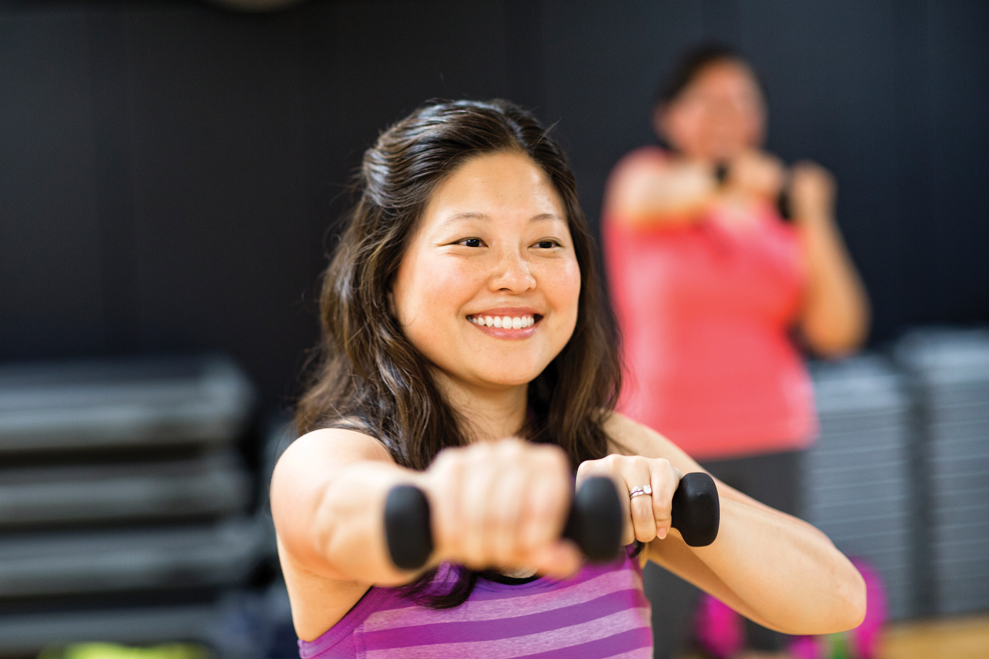 Woman working with dumbbells and smiling at YMCA group fitness class Woman working with dumbbells and smiling at YMCA group fitness class