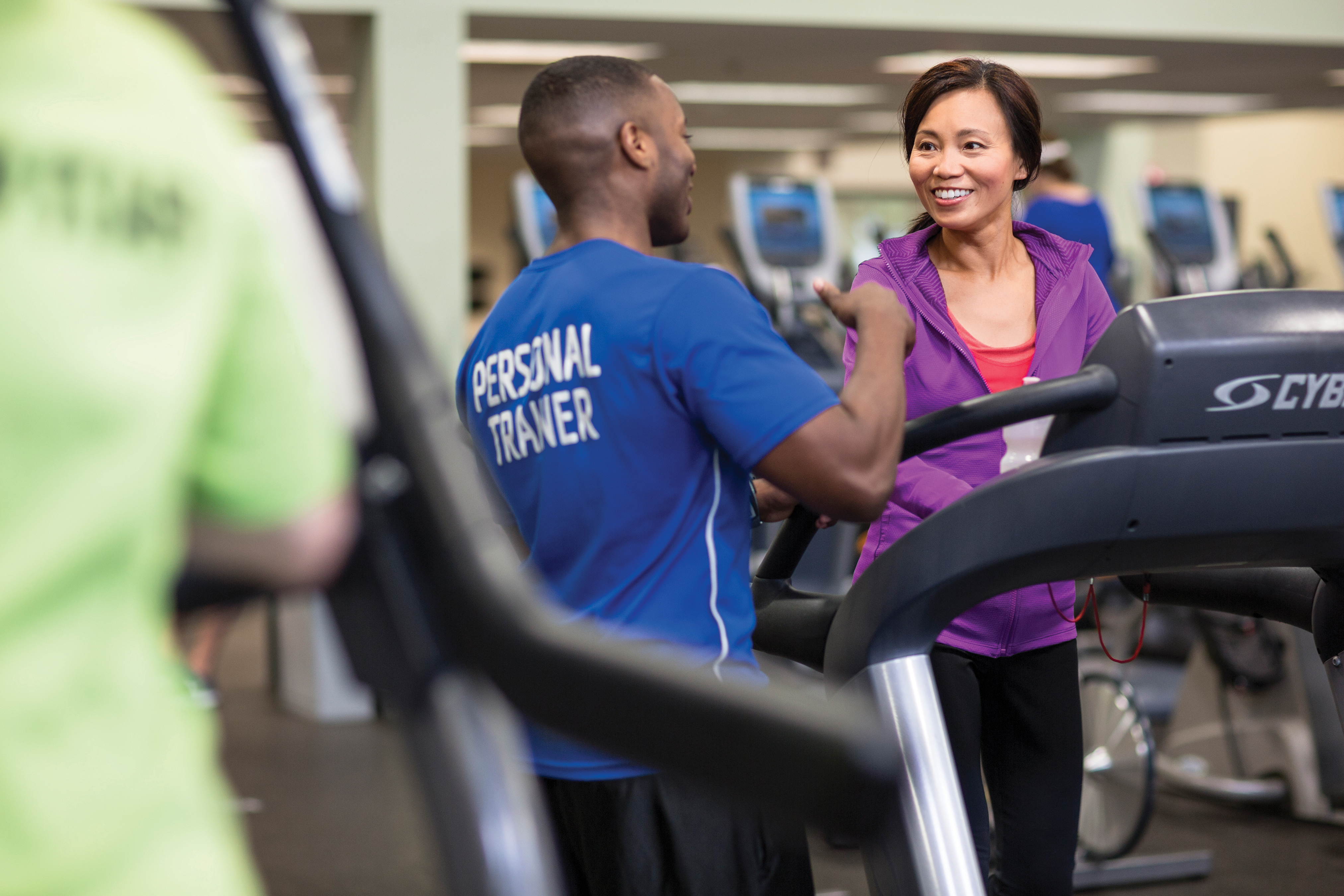 Woman walks on treadmill while personal trainer supervises Woman walks on treadmill while personal trainer supervises
