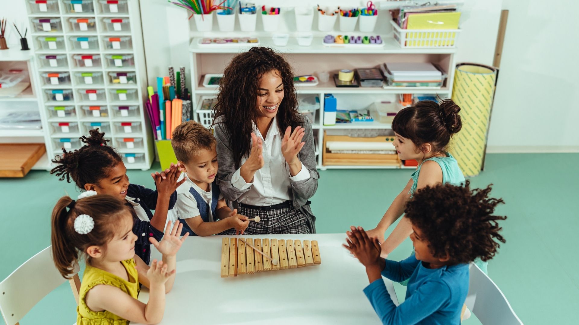 Woman leading group of children sitting at table in hand clapping Woman leading group of children sitting at table in hand clapping
