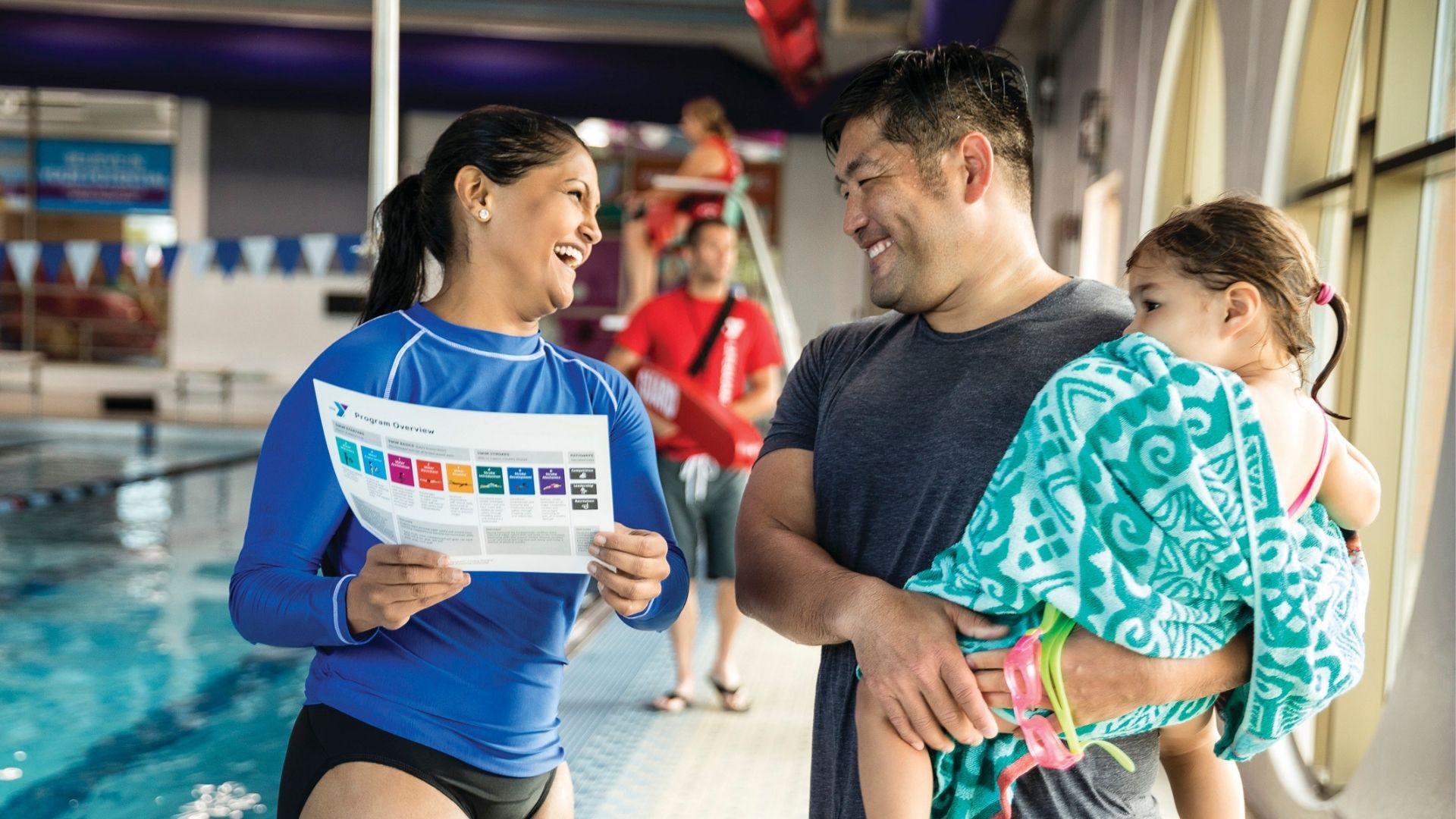 Female swim instructor talking with man holding young daughter Female swim instructor talking with man holding young daughter
