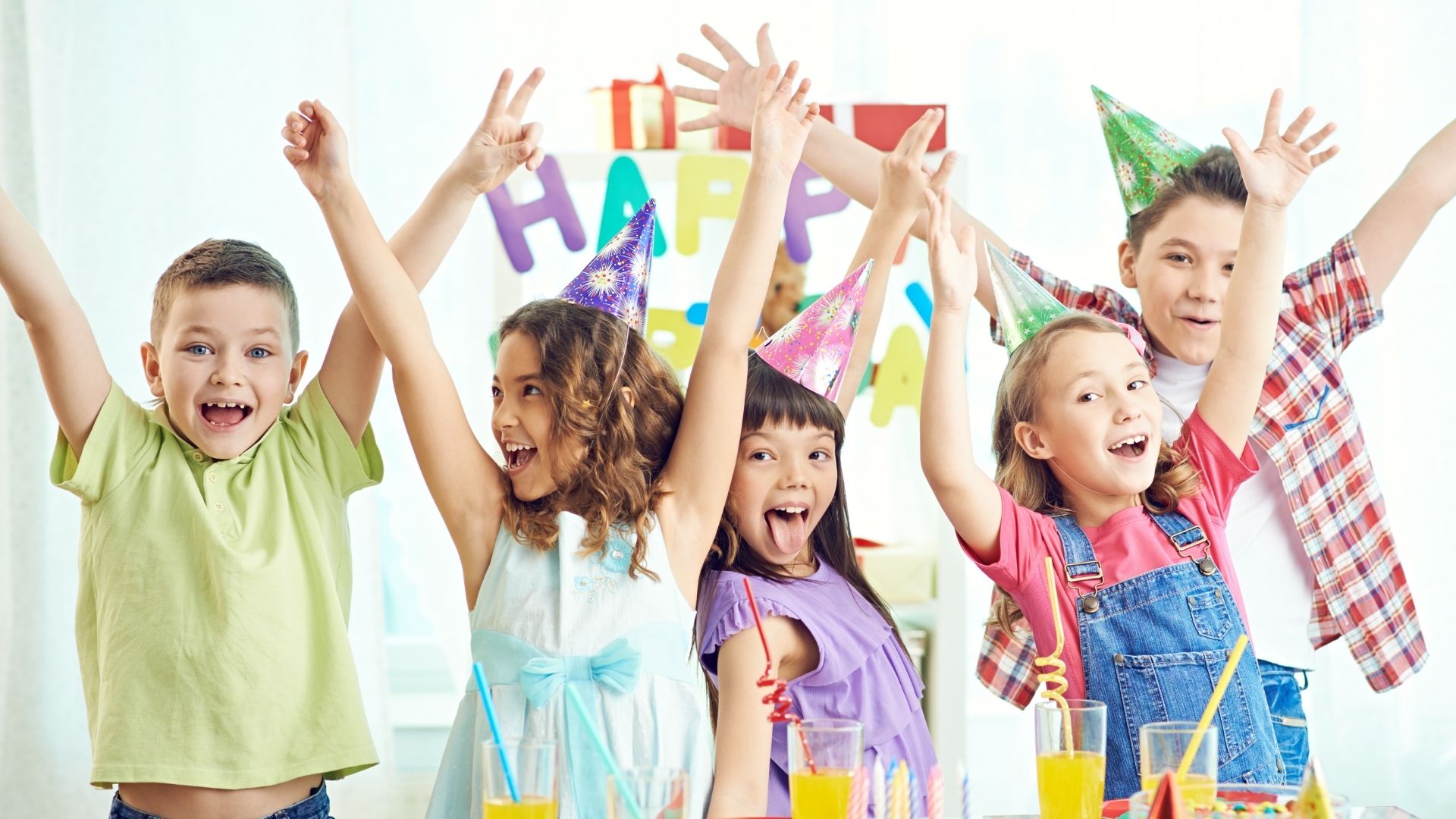 Group of kids in party hats with hands raised celebrating a birthday Group of kids in party hats with hands raised celebrating a birthday