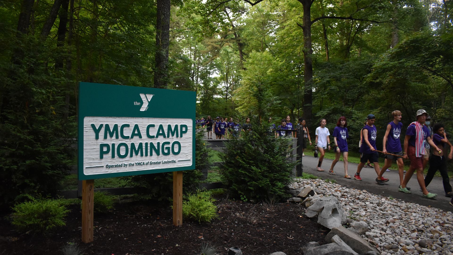 Group of campers walking past the YMCA Camp Piomingo welcome sign Group of campers walking past the YMCA Camp Piomingo welcome sign