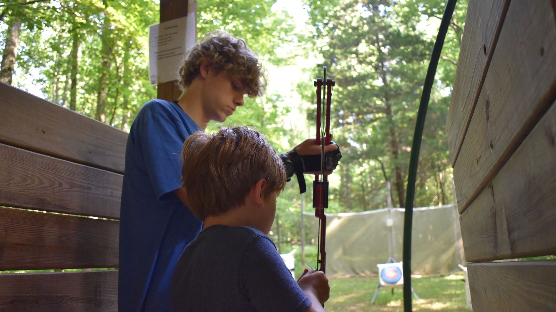 Camp counselor teaching a young camper how to do archery Camp counselor teaching a young camper how to do archery
