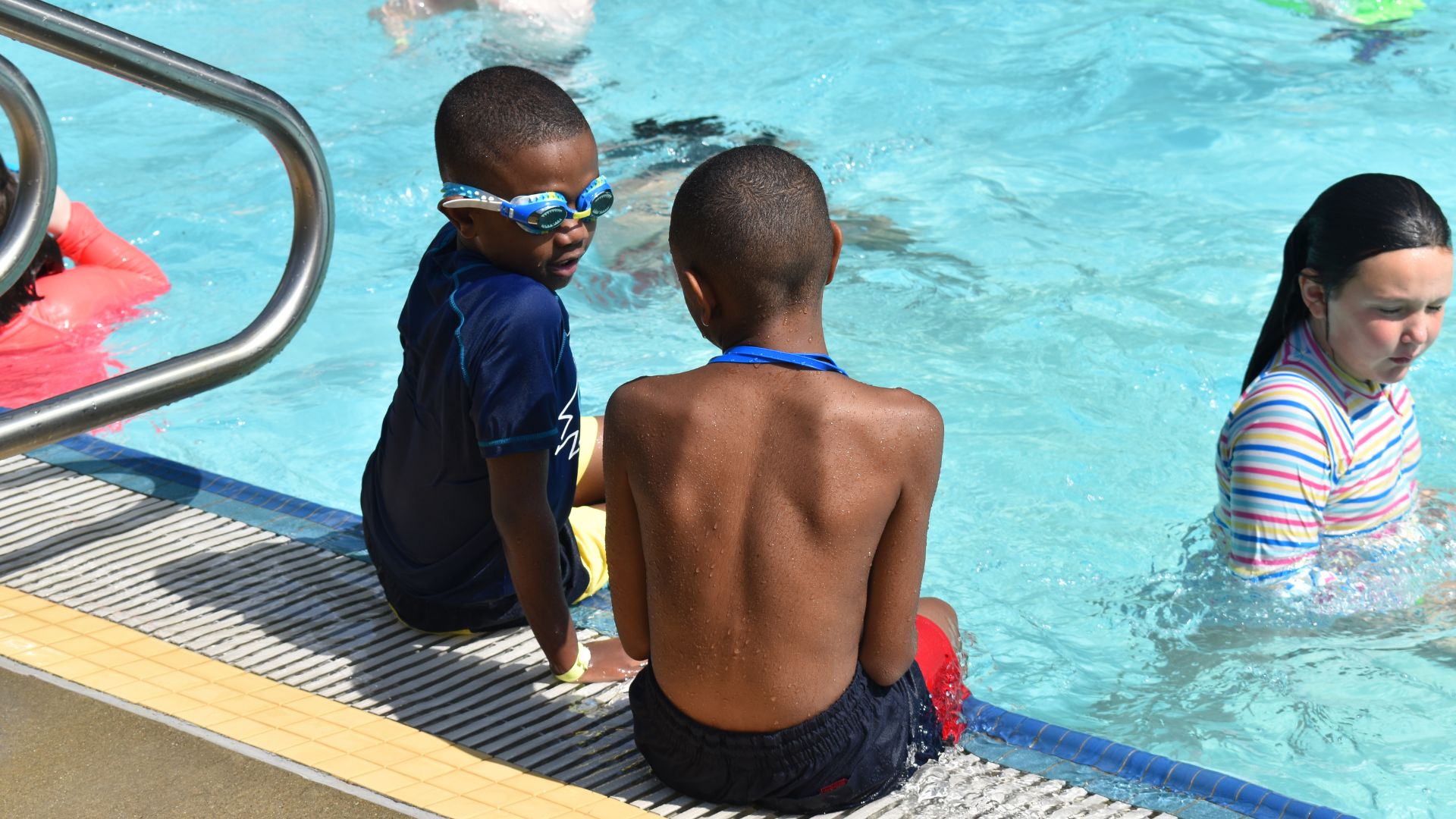 Two children sitting on the pool deck with their feet in the water Two children sitting on the pool deck with their feet in the water