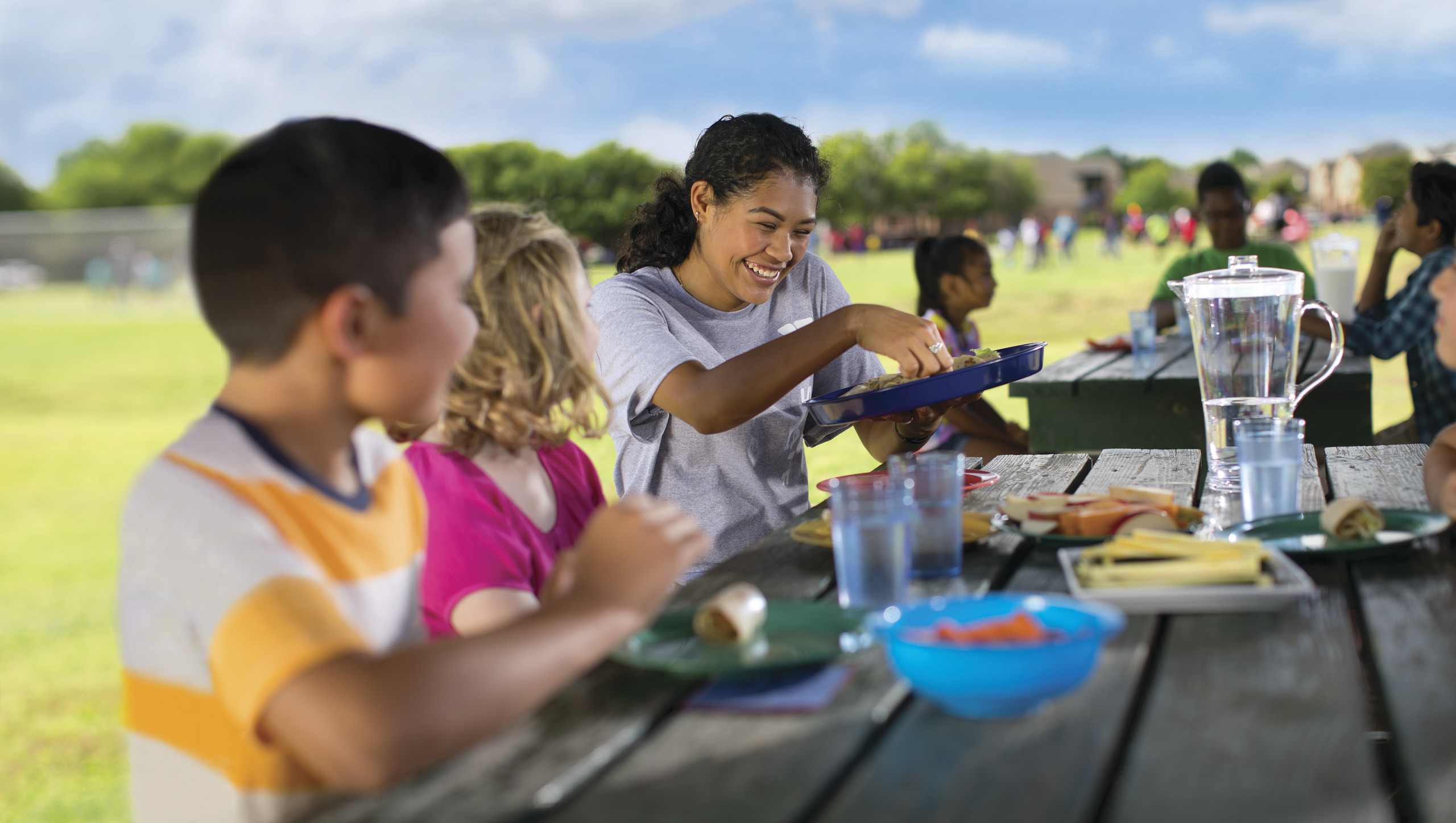 Woman serving food to two children sitting in a picnic table Woman serving food to two children sitting in a picnic table