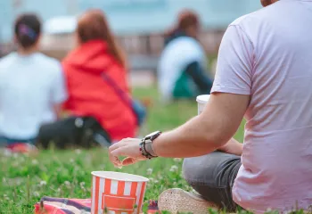 Man sitting on blanket in grass eating popcorn watching a movie outdoors