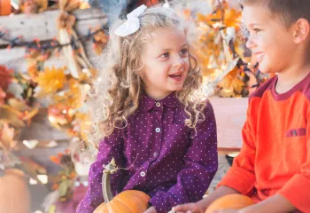 Kids holding pumpkins sitting outside in the fall