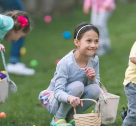 3 smiling young children hunting Easter eggs outdoors