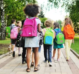 Group of children in backpacks walking on sidewalk as they go back to school