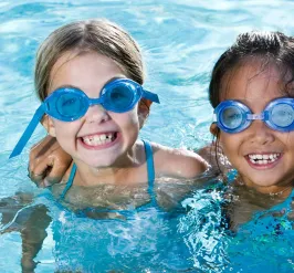Two smiling kids in swim goggles in the pool at the YMCA