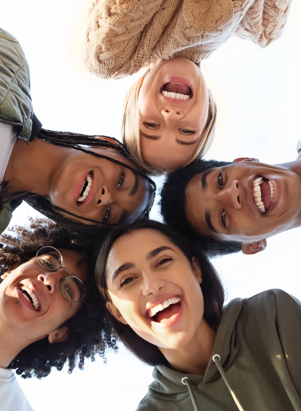 Five smiling teens standing in a circle, looking down at the camera