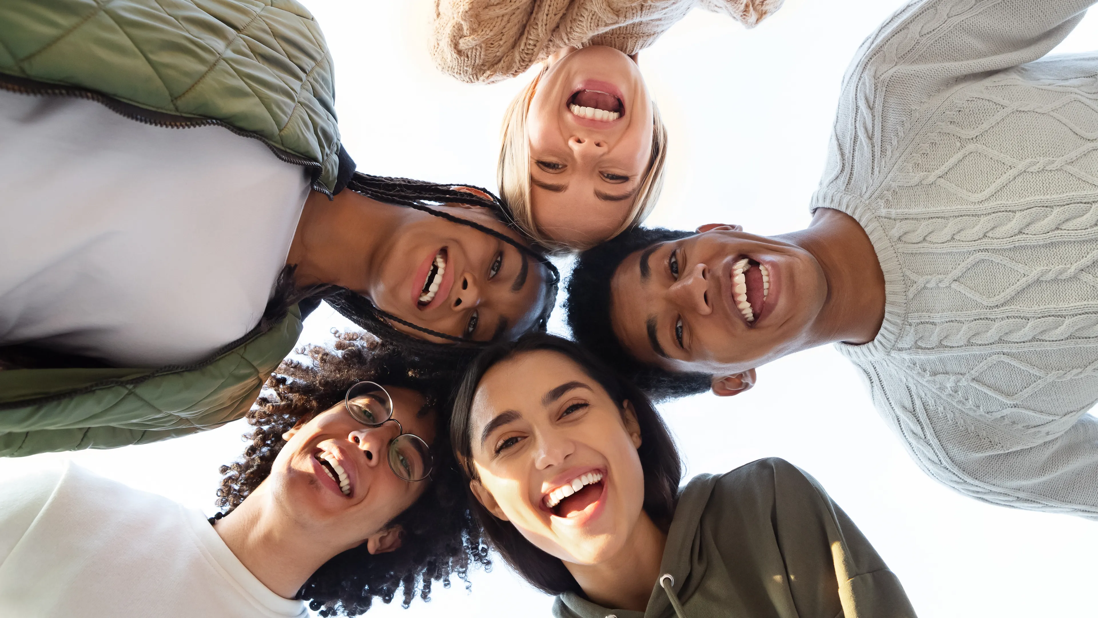 Five smiling teens standing in a circle, looking down at the camera