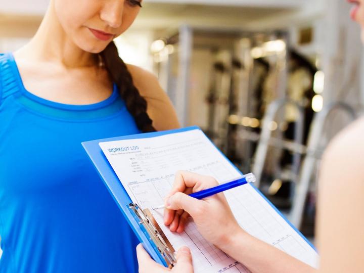 Trainer writing notes on clipboard as woman reads along