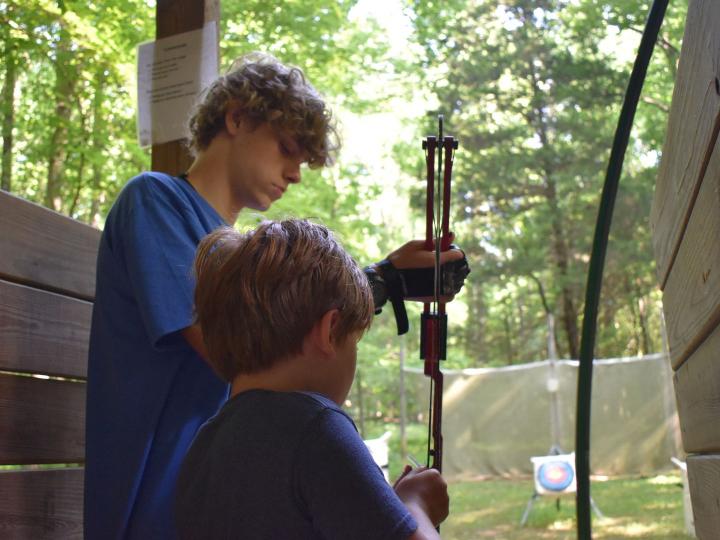 Camp counselor teaching a young camper how to do archery