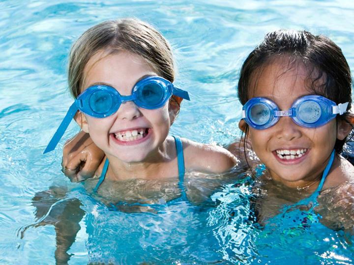 Two smiling kids in swim goggles in the pool at the YMCA