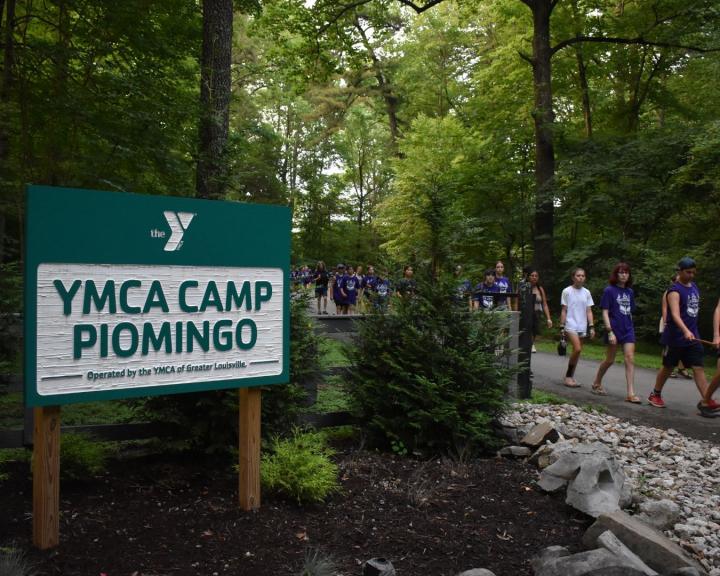 Group of campers walking past the YMCA Camp Piomingo welcome sign Group of campers walking past the YMCA Camp Piomingo welcome sign