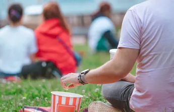 Man sitting on blanket in grass eating popcorn watching a movie outdoors