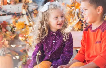 Kids holding pumpkins sitting outside in the fall