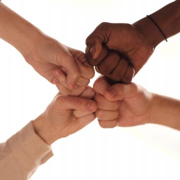 Four hands fist-bumping together in a sign of teamwork Four hands fist-bumping together in a sign of teamwork