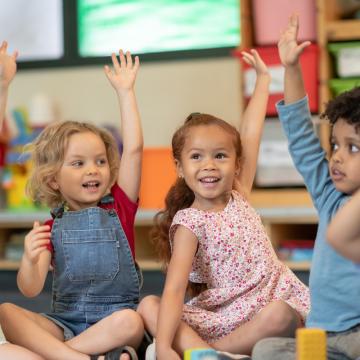 Kids raising their hands in YMCA child care program Kids raising their hands in YMCA child care program