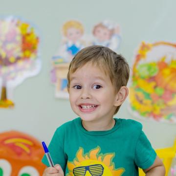 Smiling young boy sitting at table with art supplies and globe Smiling young boy sitting at table with art supplies and globe