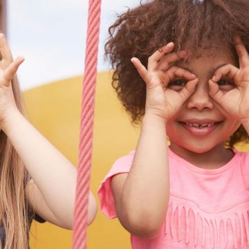Two smiling young girls acting like they are wearing glasses by using their hands Two smiling young girls acting like they are wearing glasses by using their hands
