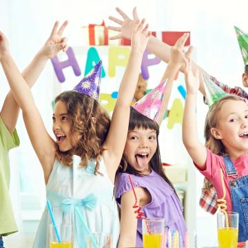 Group of kids in party hats with hands raised celebrating a birthday Group of kids in party hats with hands raised celebrating a birthday