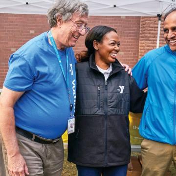 3 YMCA volunteers standing together at a volunteer tent 3 YMCA volunteers standing together at a volunteer tent