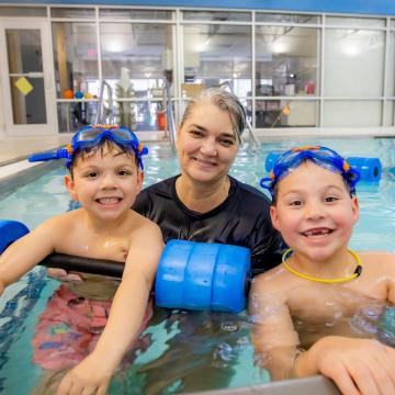 Swim instructor in pool with two smiling young boys Swim instructor in pool with two smiling young boys