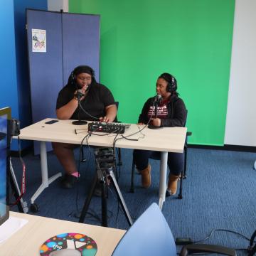 2 teens sitting at a desk recording a podcast 2 teens sitting at a desk recording a podcast