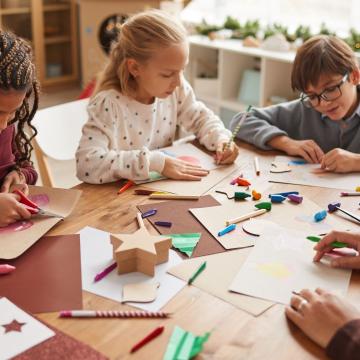 2 girls and a boy sitting a table doing crafts 2 girls and a boy sitting a table doing crafts