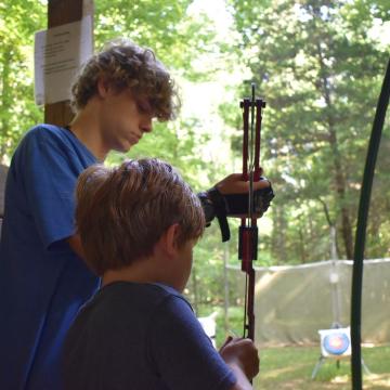 Camp counselor teaching a young camper how to do archery Camp counselor teaching a young camper how to do archery