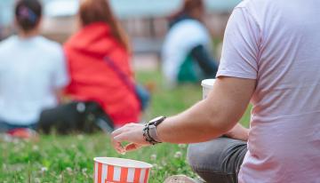 Man sitting on blanket in grass eating popcorn watching a movie outdoors