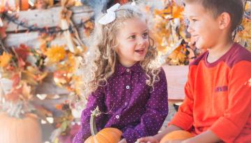 Kids holding pumpkins sitting outside in the fall